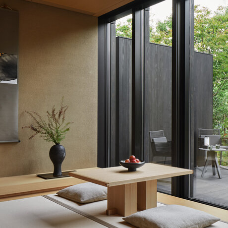 Susuki Room at Aman Kyoto, with wooden platform seating, ikebana arrangement, and garden views through glass doors.