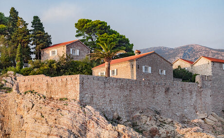 Sveti Stefan Suite at Aman Sveti Stefan, Montenegro: terracotta-roofed buildings perched on a rocky islet at dusk.