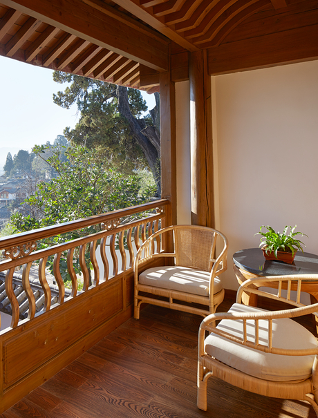Wooden balcony at Amandayan with carved railings, comfortable seating, and mountain views through open doors.