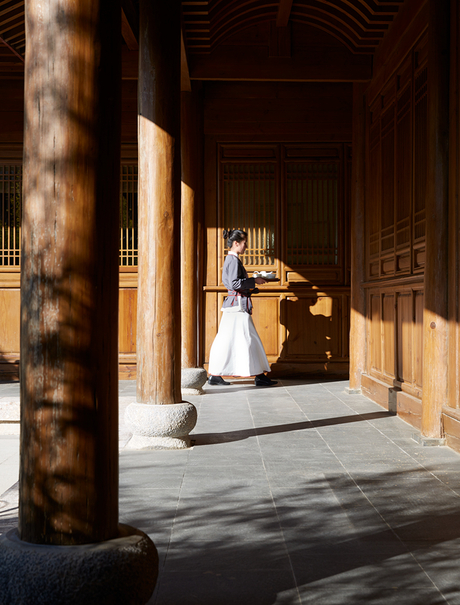 Woman in traditional dress standing beneath wooden columns at Amandayan.