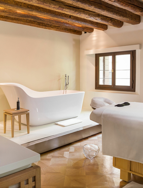 Principal bedroom with freestanding bath at Aman Venice, featuring wooden beams and terracotta flooring.