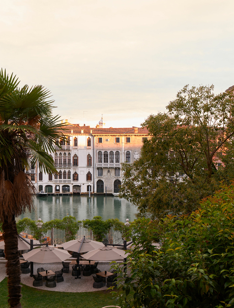 Terracotta palazzo overlooking a Venice canal, framed by palm and garden foliage at Aman Venice.