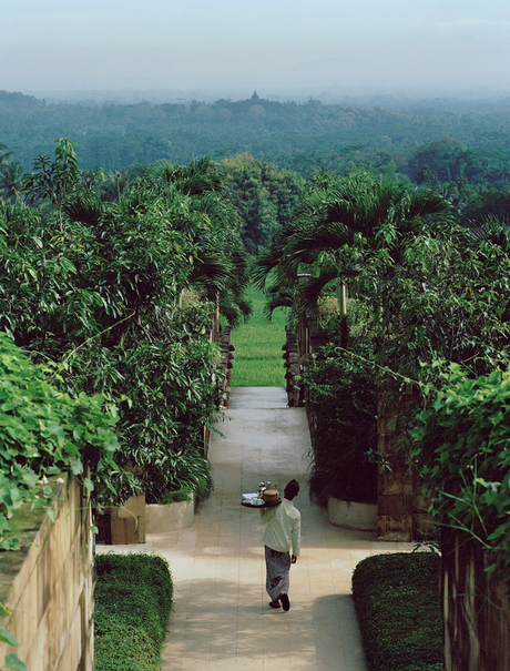Amanjiwo guest walking through manicured garden pathway towards misty volcanic landscape.