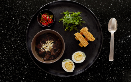 安缦齐和度假村的餐点展示，黑色餐盘上有汤碗、面条、蛋类和新鲜配菜。