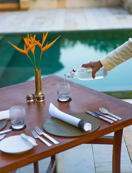 Dining table set with place settings and bird of paradise flower, overlooking pool at Amanjiwo.