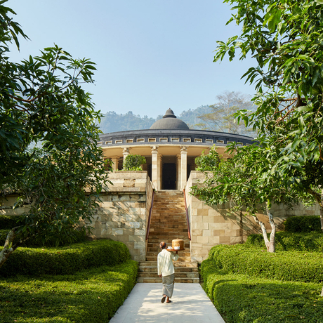 A stone pavilion with a domed roof framed by trees at Amanjiwo, with a figure walking along the central pathway.