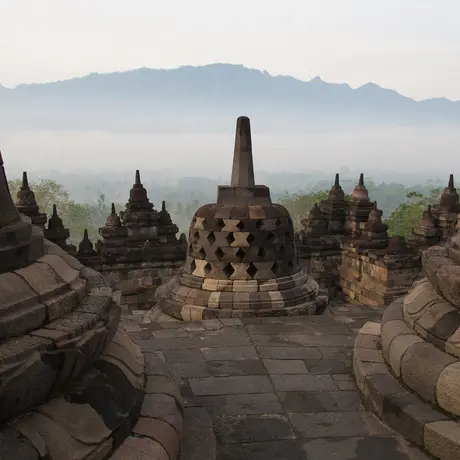 Stone stupas at Amanjiwo with misty volcanic peaks beyond, Java, Indonesia.