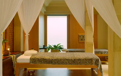 Amanjiwo spa treatment room with draped fabric ceiling, wooden pillars, and massage bed adorned with fresh flowers.
