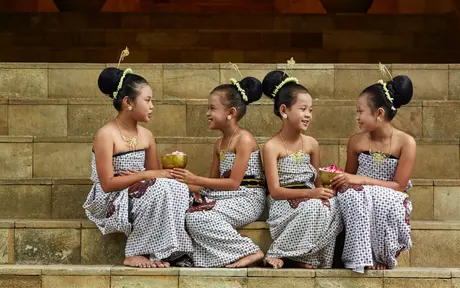 Four young dancers in traditional Javanese costume sit together on stone steps at Amanjiwo.