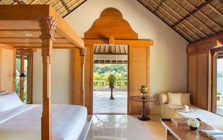 Amankila resort interior with wooden pavilion, draped bed and views towards tropical gardens.