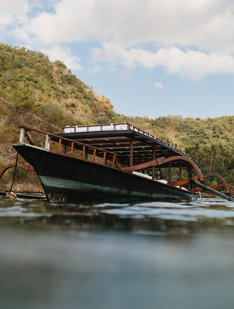 Traditional wooden boat moored in calm waters at Amankila, surrounded by lush hillside vegetation.