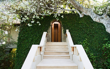 Cream stone staircase leading to wooden doors at Amankila, framed by verdant climbing ivy and white flowering vines.