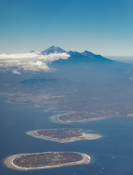 Aerial view of Amanwana's island setting, with volcanic mountain rising above clouds and surrounding turquoise waters.