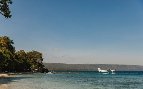 Moored boat off a sandy beach at Amanwana, with forested shoreline and calm turquoise waters.