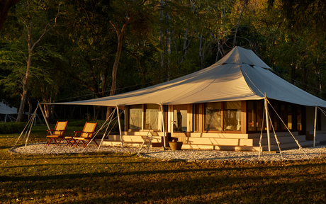Amanwana canvas tent glowing warmly at dusk, surrounded by forest trees.