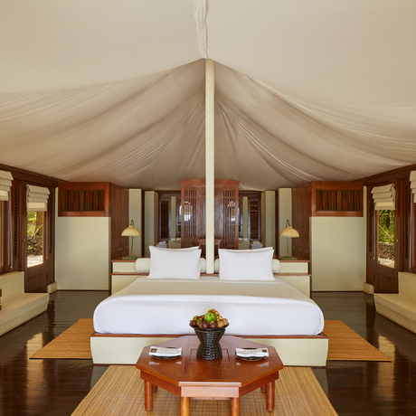 Amanwana villa bedroom with draped canvas ceiling, four-poster bed and wooden furnishings.