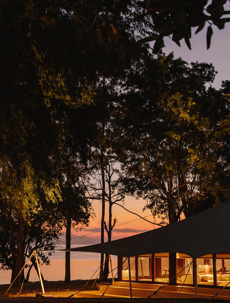 Amanwana pavilion illuminated at dusk beneath sheltering trees and fading sky.