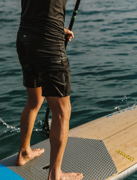 Person standing on paddleboard at Amanwana, viewed from waist down, ocean in background.
