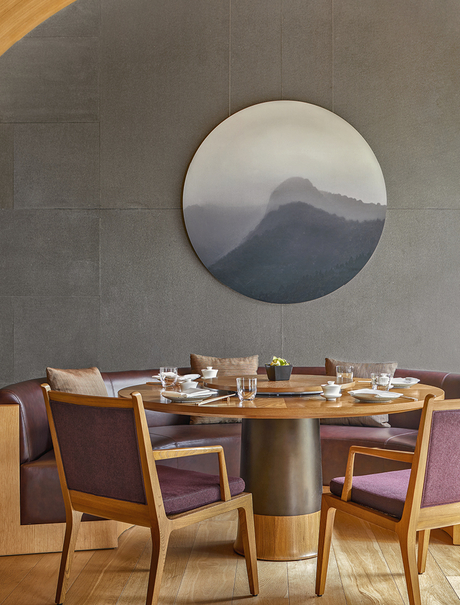 Dining table and wooden chairs beneath a circular window framing mountain views at Amanyangyun.