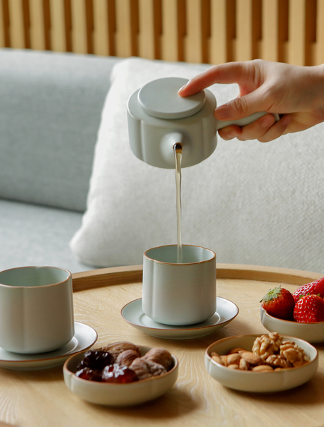 Hand pouring tea at Amanyangyun, with ceramic cups and bowls of nuts and berries on table.
