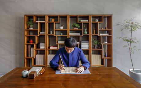 Woman in blue shirt seated at wooden desk in front of built-in shelving at Amanyangyun.