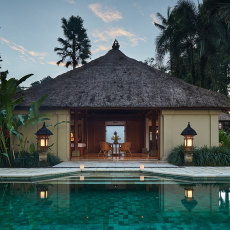 Amandari suite with thatched roof pavilion reflected in still pool at dusk, Bali.