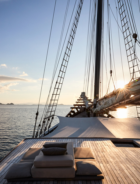 Wooden deck of a sailing vessel at Amandira, Indonesia, with rigging and sails visible at sundown over calm waters.
