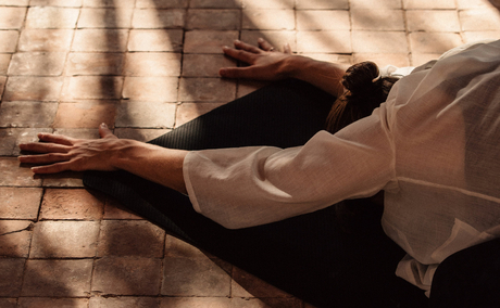Wellness guest practising yoga at Amanjena, arms extended in sunlit space.