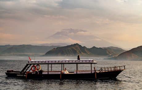 Wooden boat floating on calm water at Amankila resort, with misty mountains in the background at dusk.