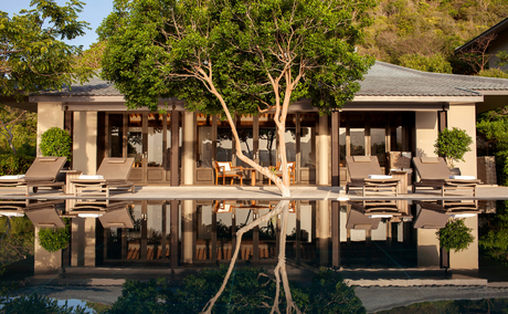 Amanoi's waterfront pavilions reflected in still waters, framed by mature trees.