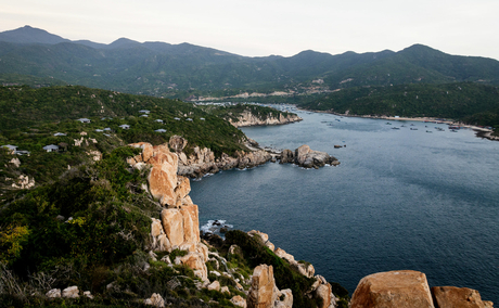 Amanoi's clifftop setting overlooks a tranquil bay with forested coastline and rocky outcrops.