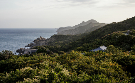 Amanoi's coastal landscape with forested hillside sloping towards calm sea and distant mountains.