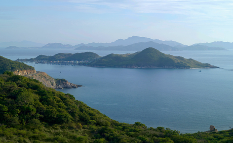 Amanoi's coastal vista overlooking forested hillsides and tranquil blue waters with distant mountains.