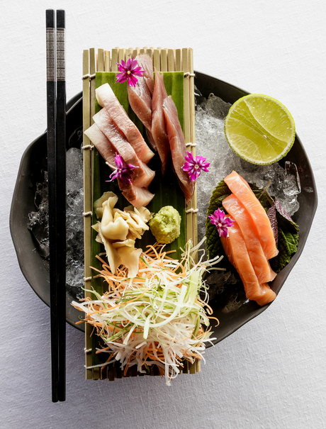 Amanoi dining: plated Asian dish with noodles, vegetables and seafood, garnished with lime slice and chopsticks.