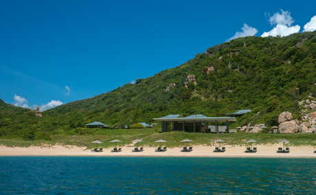 Amanoi's private beach with sun loungers along the shoreline, lush hillside and turquoise waters.