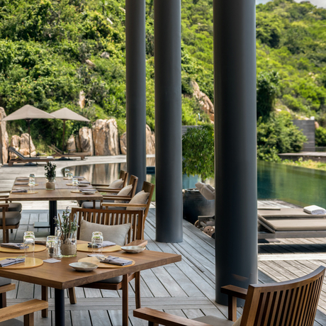Wooden deck at Amanoi with dining furniture and water views through supporting columns.
