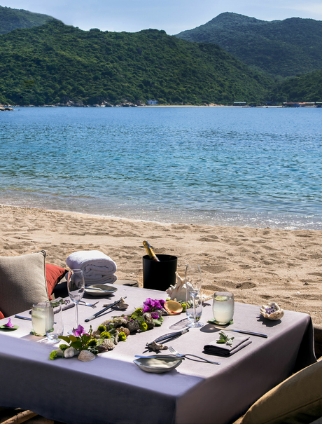 Beachfront dining setup at Amanoi with turquoise waters and forested hills beyond.