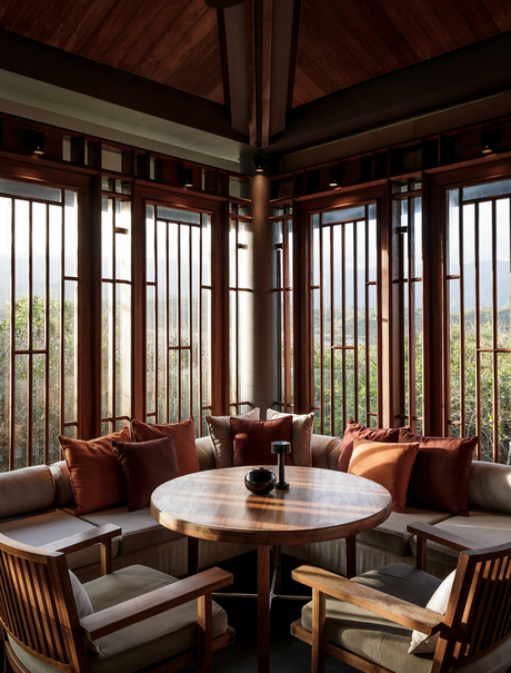 Amanoi gallery space with round table, wooden chairs, and floor-to-ceiling windows overlooking landscape.