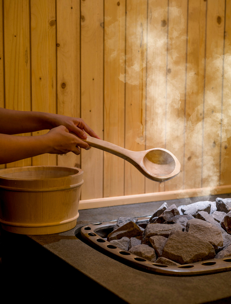 Hand pouring soup from brass ladle into bowl at Amanoi, with dried herbs and wooden backdrop.