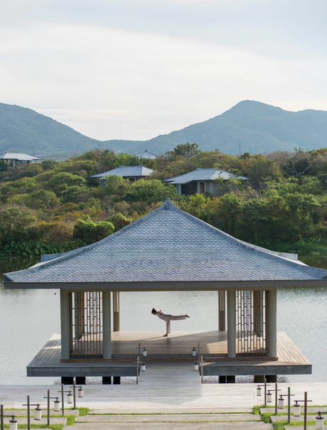 Amanoi pavilion with conical roof overlooking a lagoon and forested mountains in Vietnam.