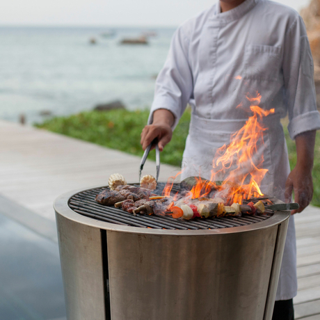 Person grilling fresh catch over an open flame at Amanoi, with coastal views beyond.