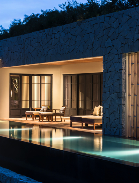 Amanoi villa with illuminated plunge pool at dusk, featuring wooden pavilion and stone facade.