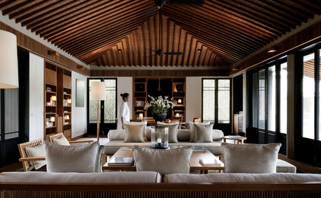 Amanoi dining venue with wooden vaulted ceiling, floor-to-ceiling windows, and round tables set for service.