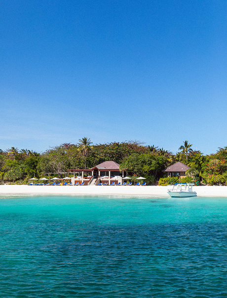 Amanpulo's beachfront with white sand, turquoise waters and hillside resort nestled among tropical vegetation.