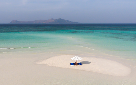 Outrigger boat anchored on white sand beach with turquoise waters at Amanpulo.