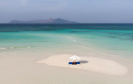 Outrigger boat anchored on white sand beach with turquoise waters at Amanpulo.