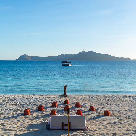 Group of people seated on Amanpulo beach facing turquoise waters with a boat and distant island.