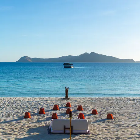 Group of people seated on Amanpulo beach facing turquoise waters with a boat and distant island.