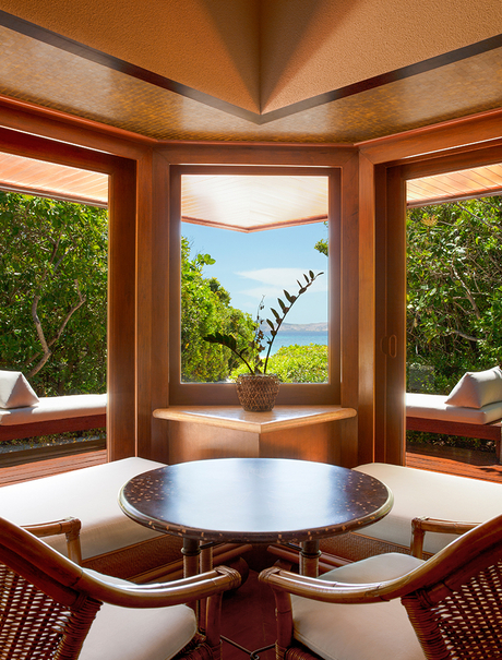 Amanpulo dining pavilion with wooden beams, round table, and views towards the sea through open windows.