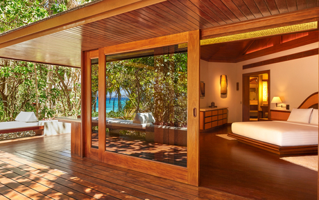 Amanpulo villa interior with sliding wooden doors opening onto a sunlit terrace, principal bedroom visible within.